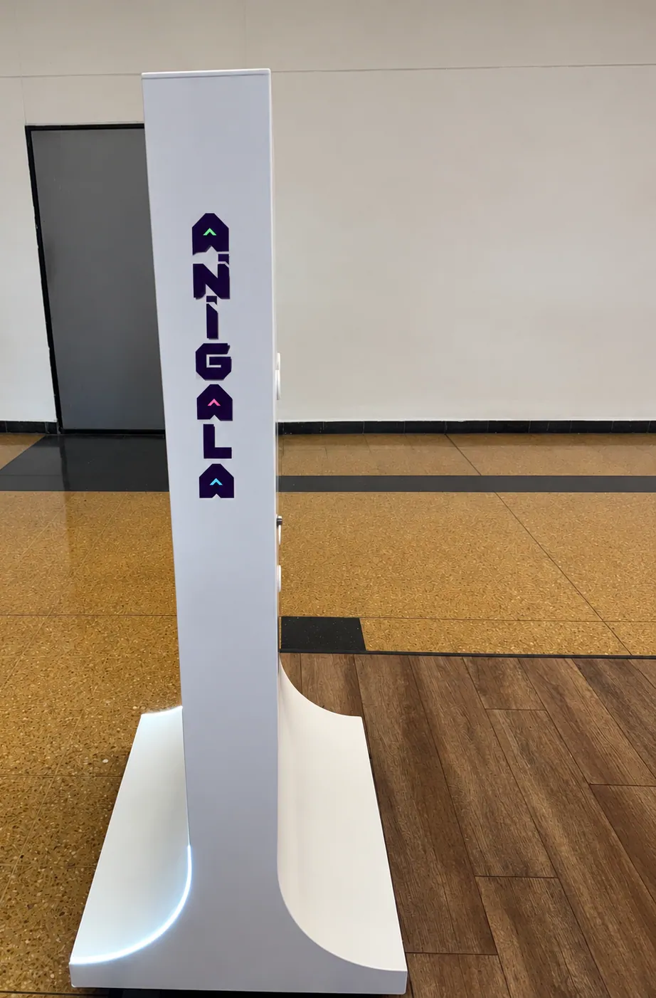 Profile view of a white Anigala totem showing its curved base and vertical logotype.